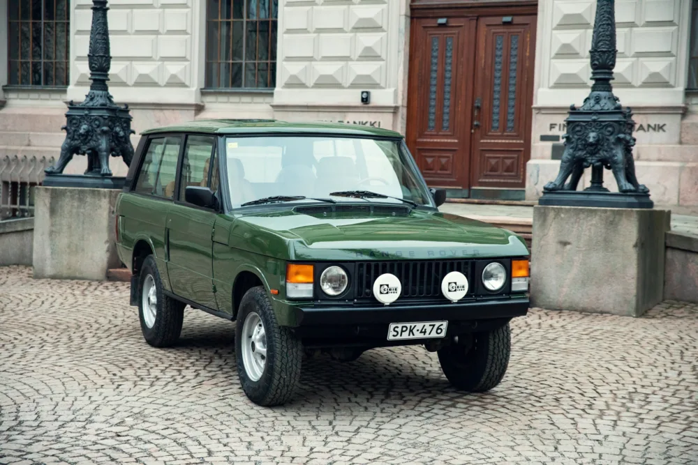 Green vintage Range Rover parked on cobblestone street.