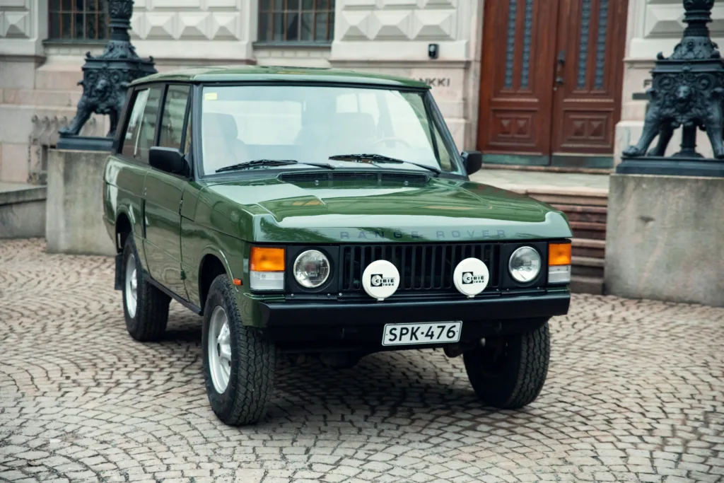 Vintage green Range Rover parked on cobblestone street.