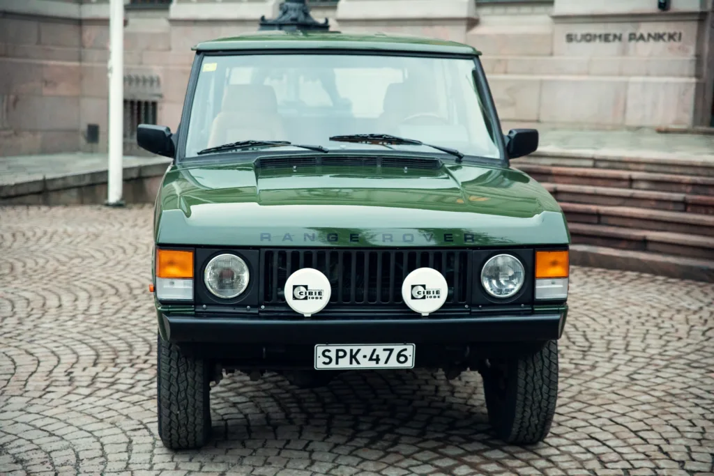 Green Range Rover classic parked on cobblestone street.