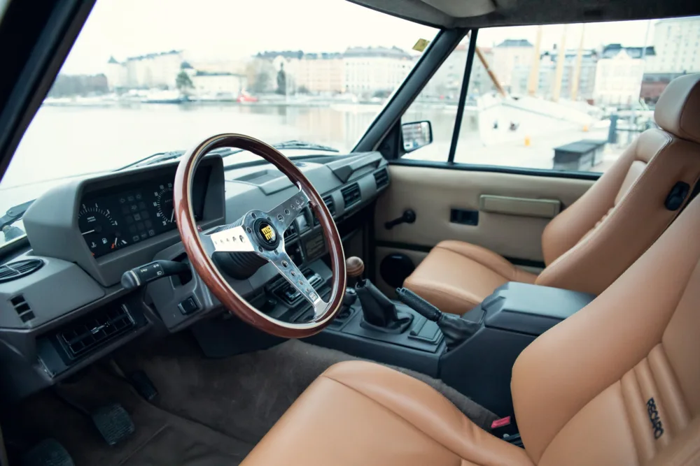 Vintage car interior with leather seats and waterfront view.