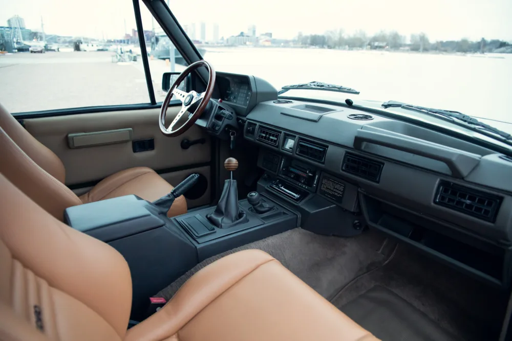 Vintage car interior, tan seats, manual transmission, waterfront view.