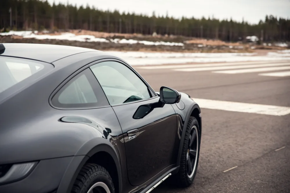 Black sports car parked on roadside with snow patches.