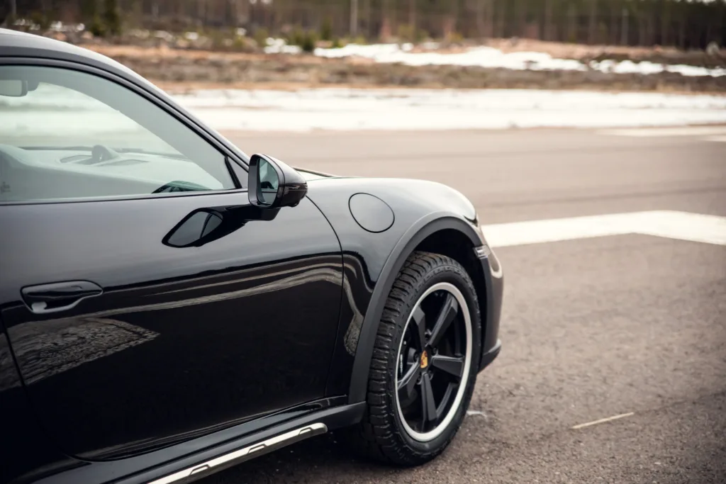 Black sports car parked on roadside with snow patches.