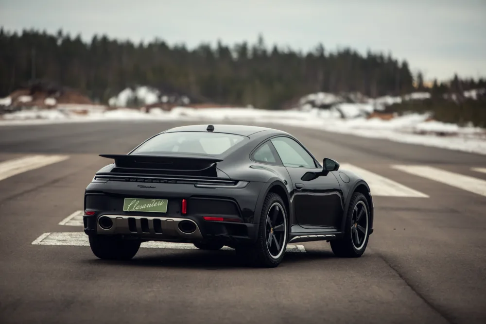 Black sports car on empty road with snowbanks.