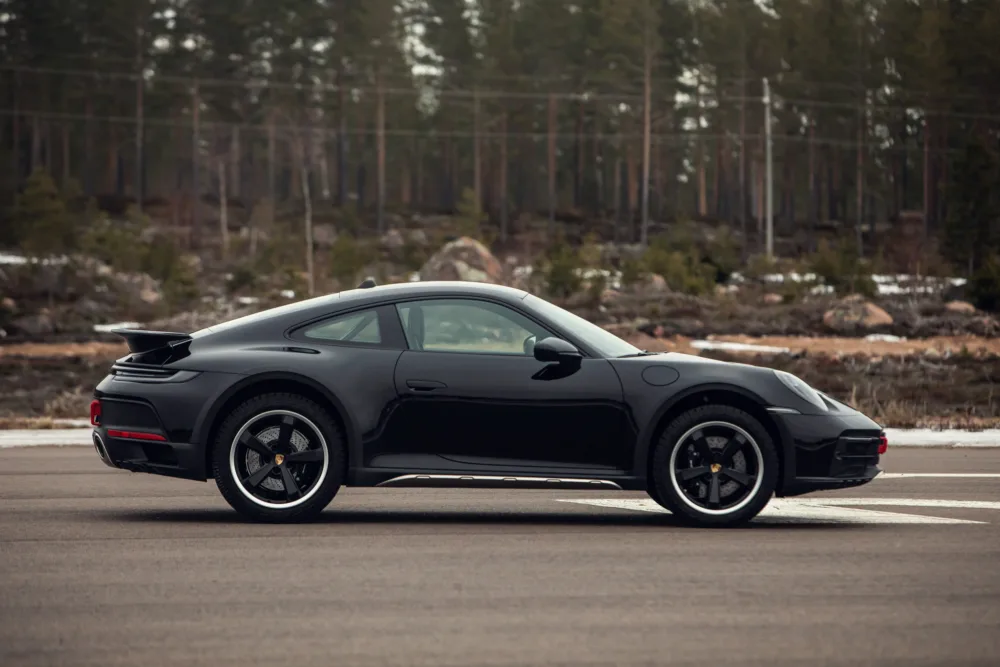 Black sports car parked on roadside in forest area.