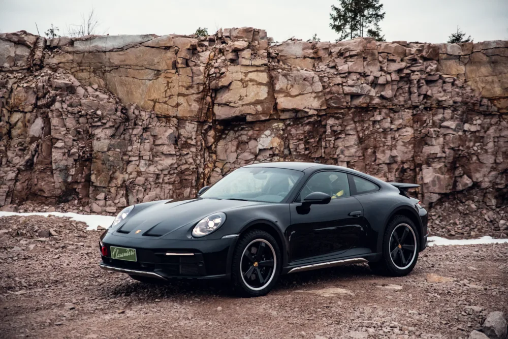 Black sports car in front of rocky quarry.