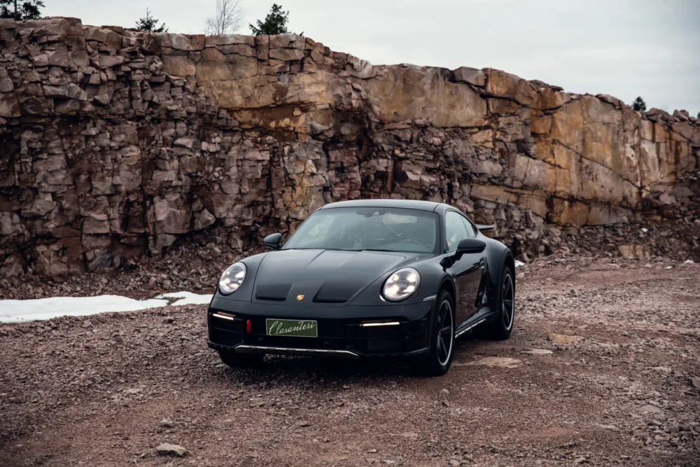 Black sports car in front of rocky cliff.