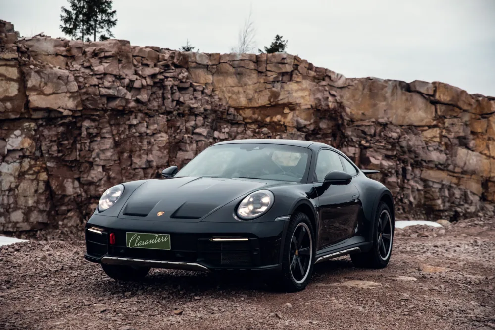 Black sports car parked in front of rocky cliff.
