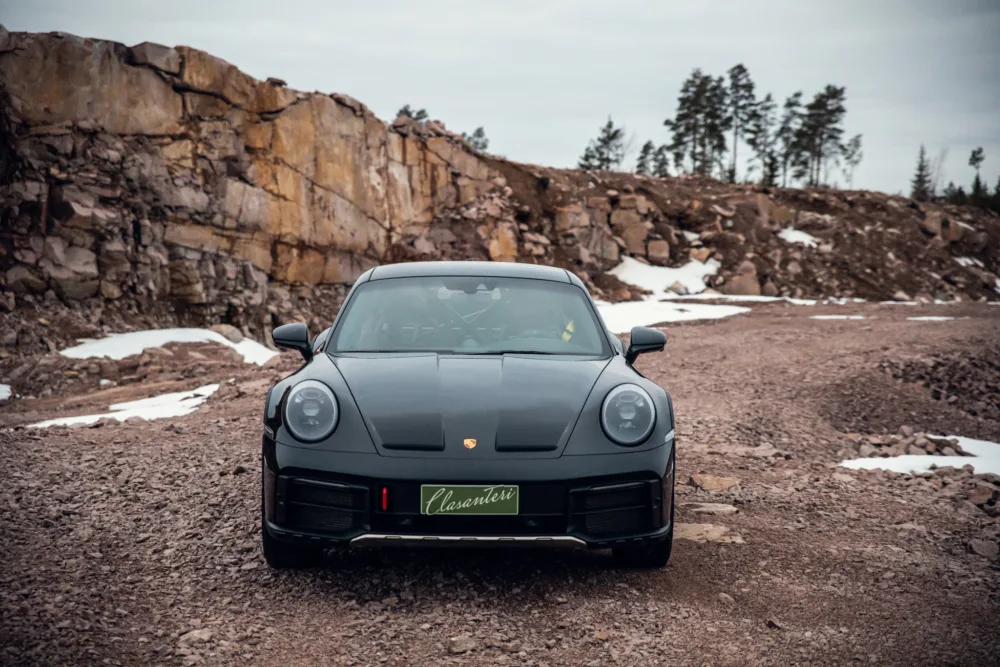 Black sports car in rocky terrain with snow patches.