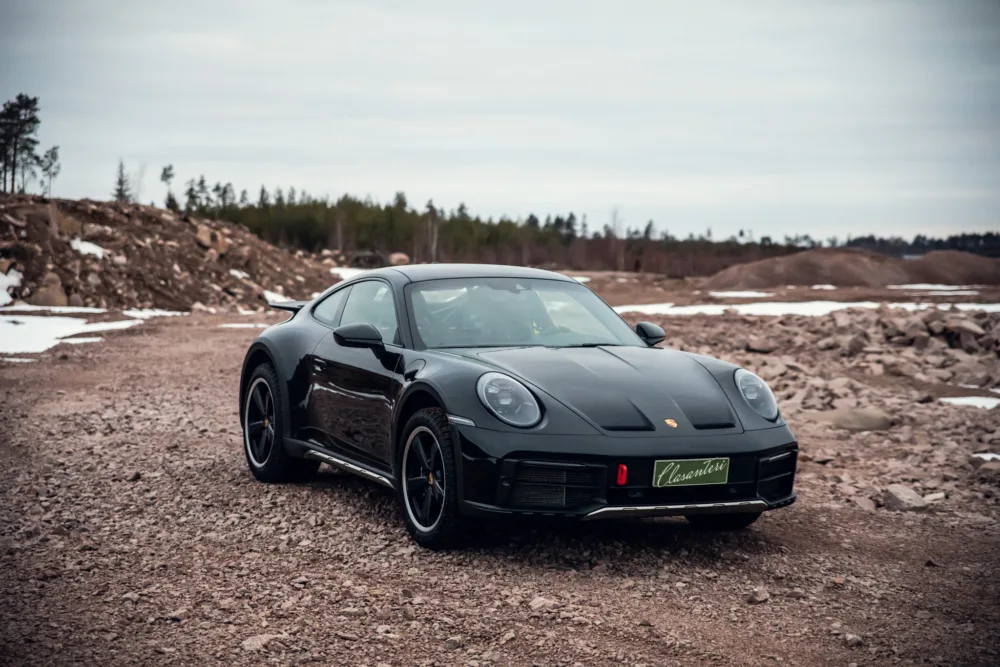 Black sports car on rugged terrain with snow patches.