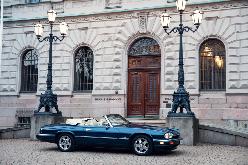 Classic blue convertible parked outside historic bank building.