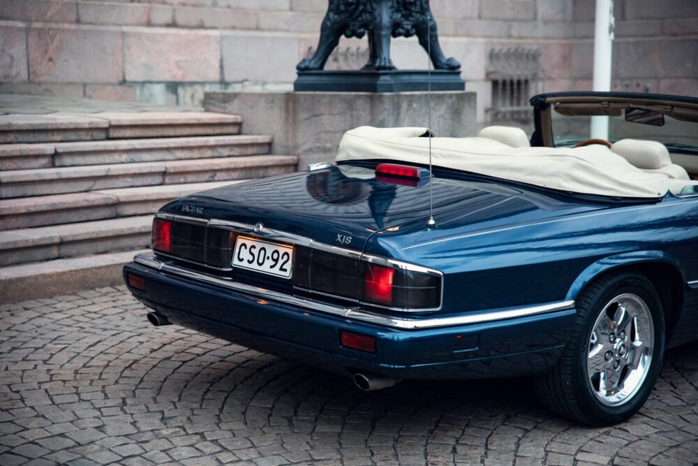 Blue Jaguar XJS convertible parked near stone steps.