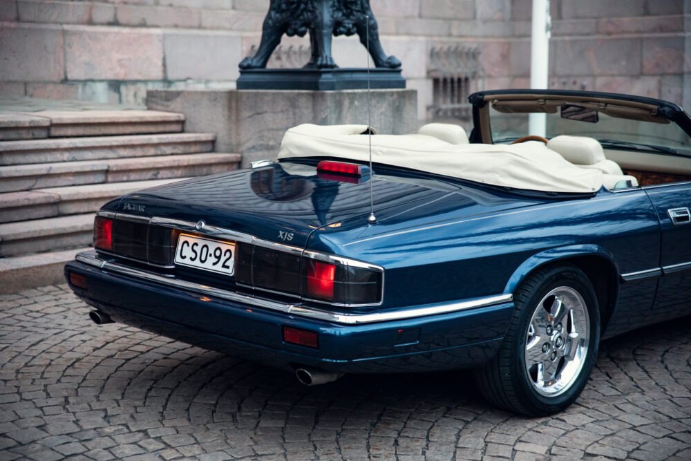 Blue Jaguar XJS convertible parked near historic building.