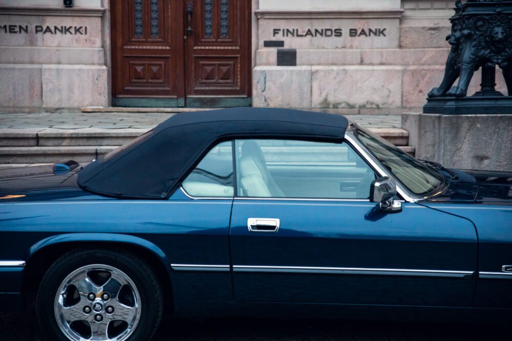 Blue convertible car parked outside Finland's Bank building.
