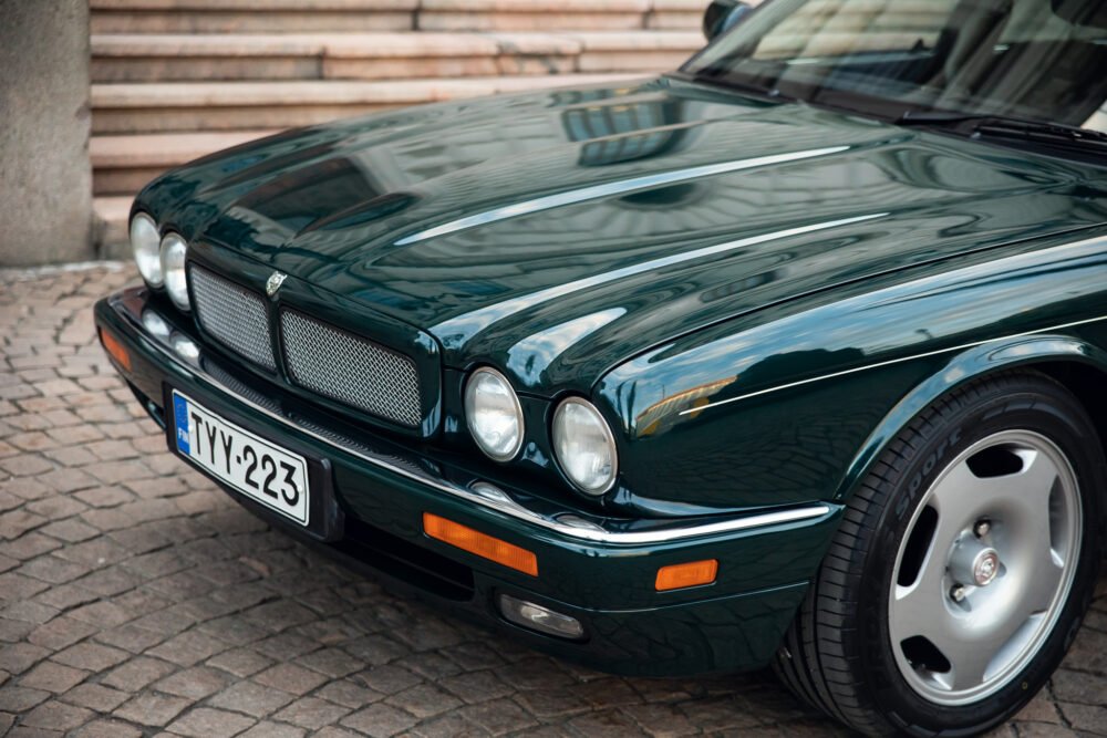 Green vintage Jaguar car parked on cobblestone street.
