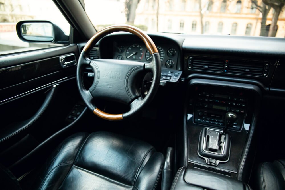 Luxury car interior with leather seats and wooden steering wheel.