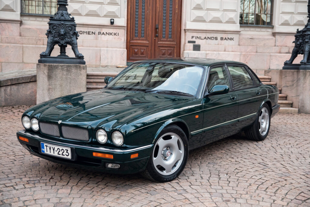 Green vintage sedan parked outside Finland's Bank building.