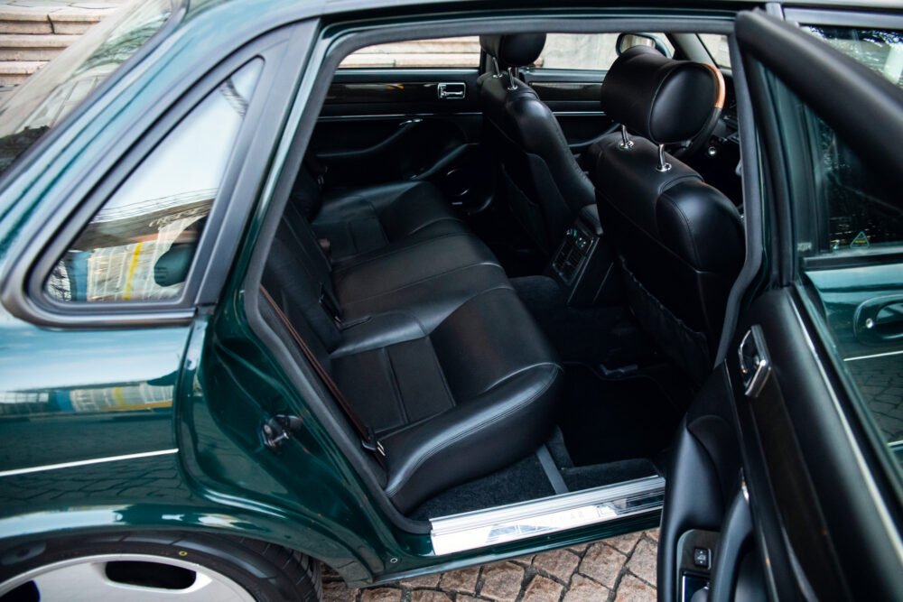 Luxurious dark green car's open door showing black interior.