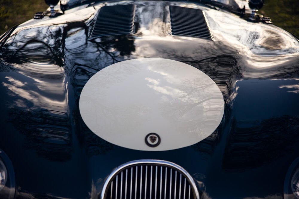 Vintage car hood and emblem, reflective surface.