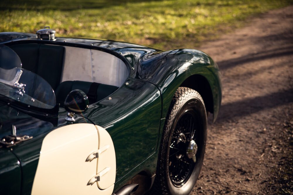 Vintage green roadster on a sunlit forest path.