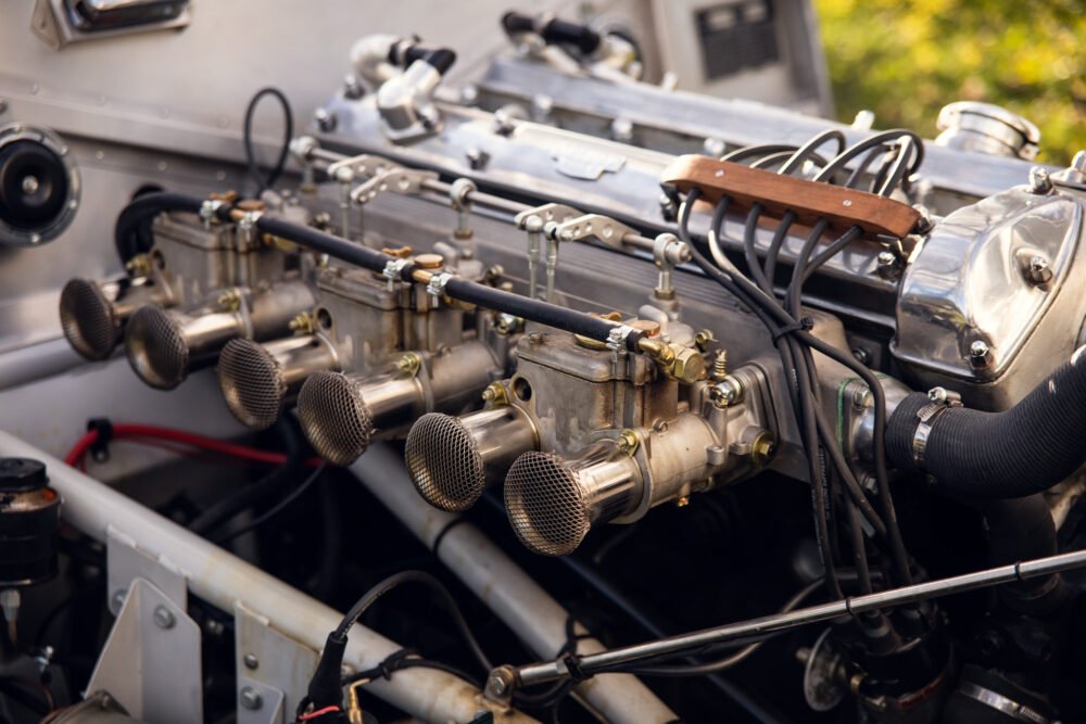 Vintage car engine with exposed carburetors and pipes.