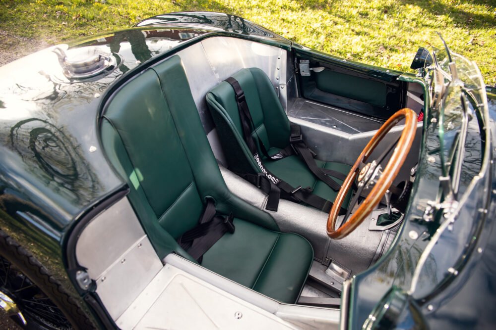 Classic sports car interior, wooden steering wheel, green upholstery.
