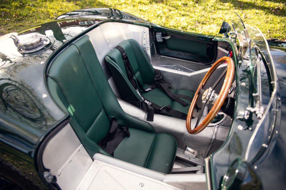 Vintage convertible car interior, wooden steering wheel, green seats.