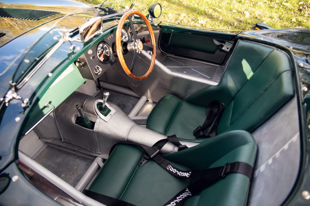 Vintage car interior with wooden steering wheel and green seats.