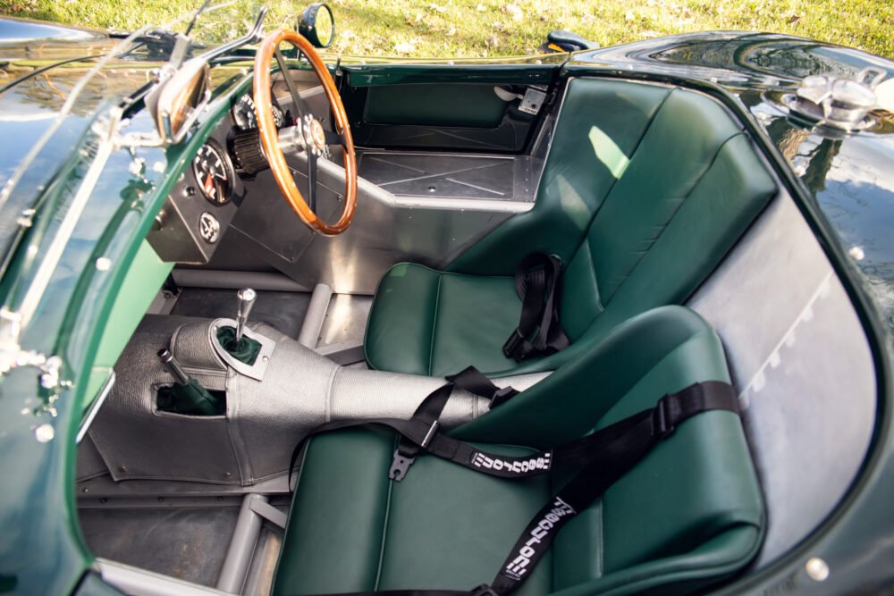 Vintage car interior with green leather seats and wooden steering wheel.
