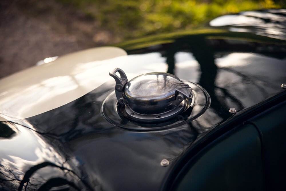Vintage car fuel cap on sleek black hood.