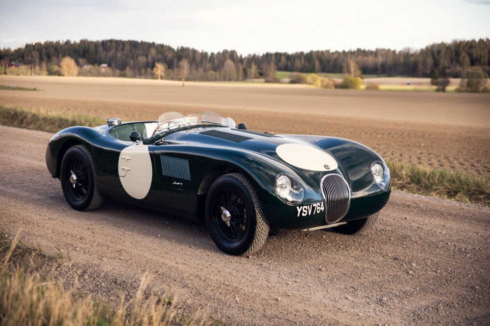 Vintage green Jaguar race car on rural road.
