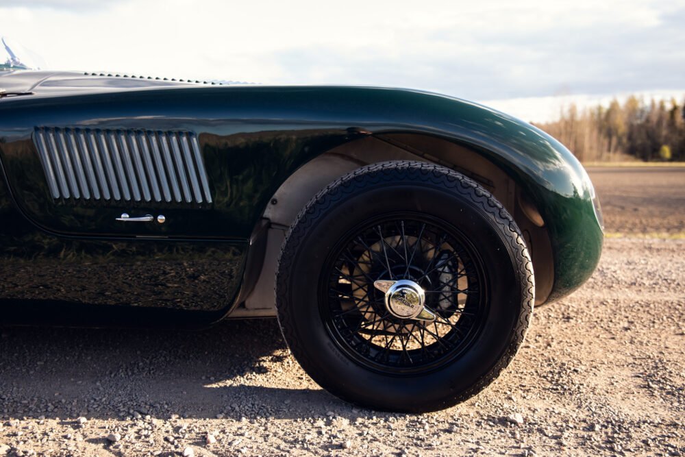 Vintage green car with detailed wheel on gravel road.