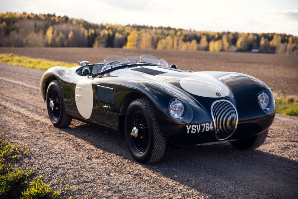 Vintage Jaguar race car on scenic country road.