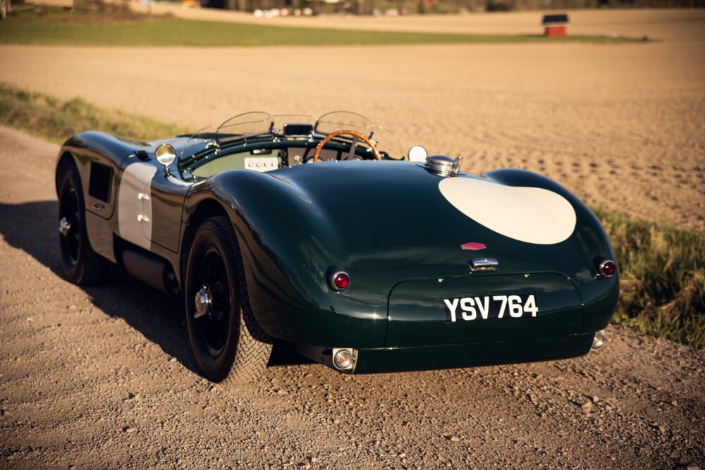 Vintage green sports car with racing number on road.