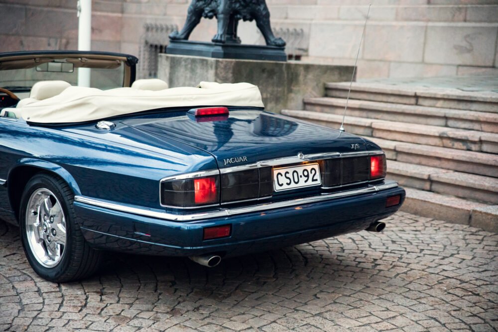 Blue Jaguar XJS convertible parked by stone stairs.