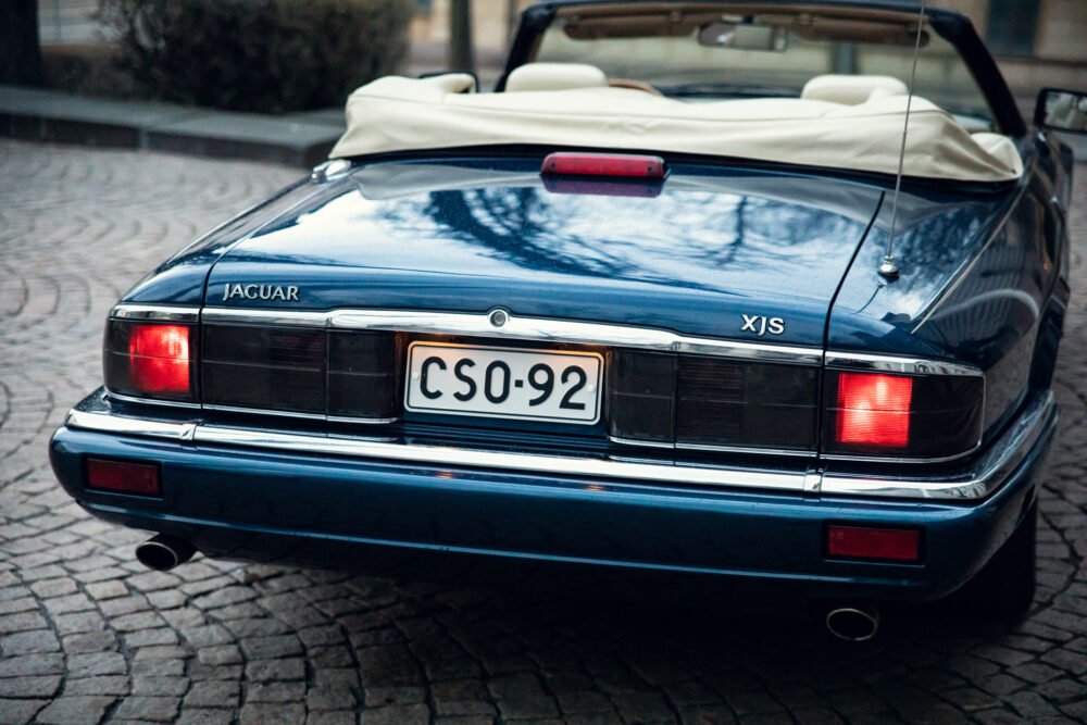 Blue Jaguar XJS convertible rear view on cobblestone street.