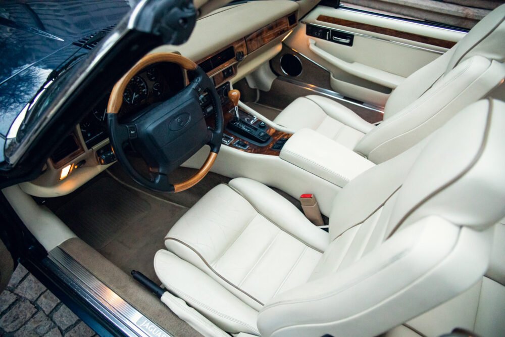 Luxury car interior with wooden dashboard and white seats.