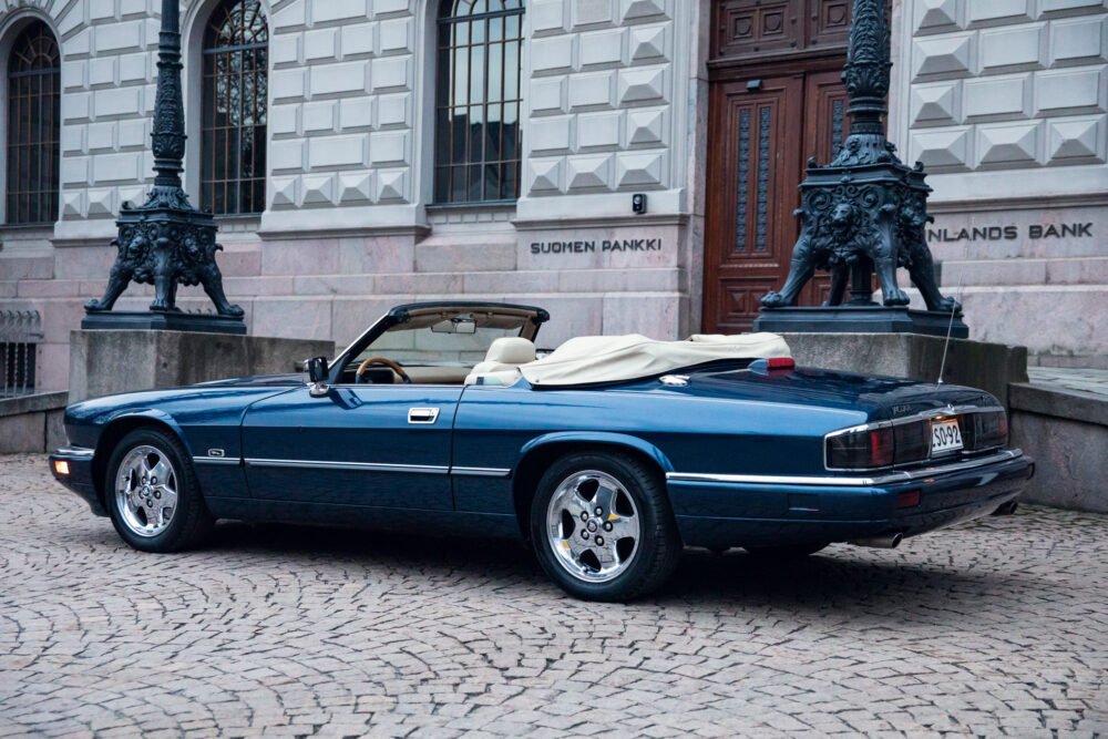 Blue convertible Jaguar parked outside historic building.