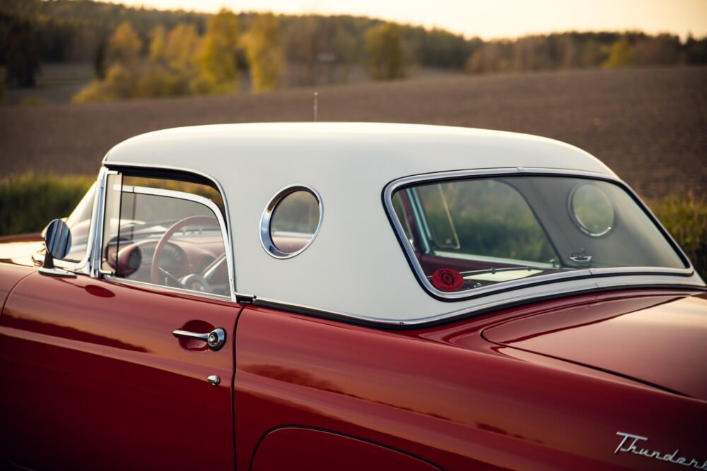 Red vintage car with circular porthole window, countryside background.