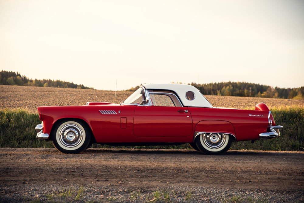 Red vintage Thunderbird car on rural road at sunset.