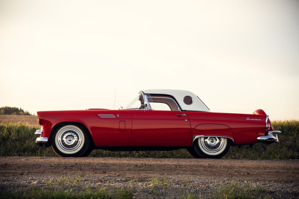 Vintage red Thunderbird car in countryside at sunset.