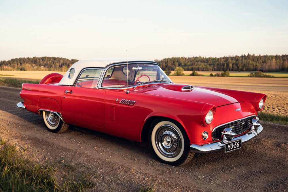Vintage red Thunderbird car on rural road at sunset.