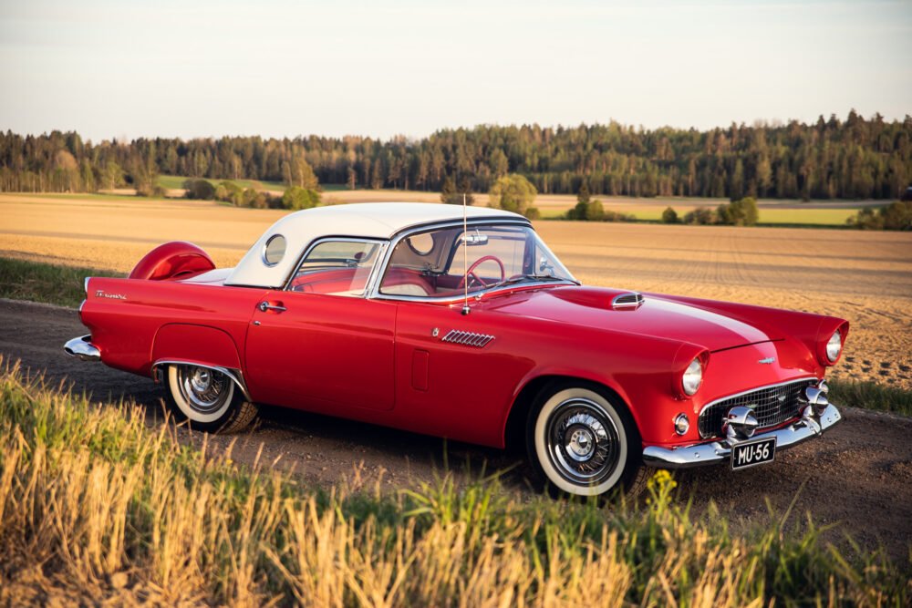 Vintage red Ford Thunderbird parked in countryside.