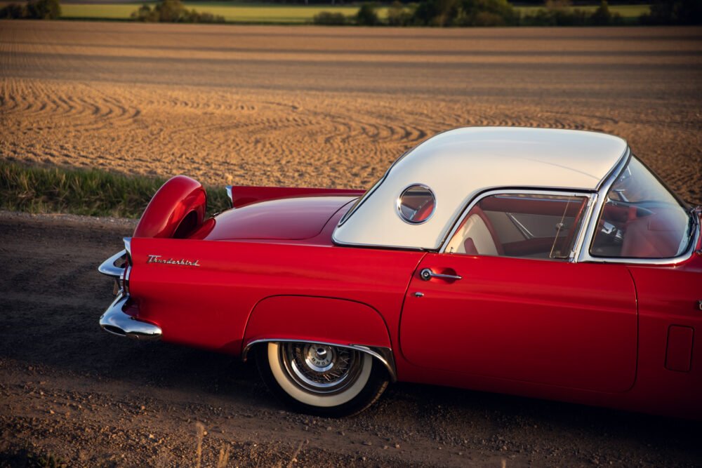 Vintage red Thunderbird car near golden field.