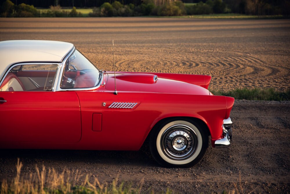 Red vintage car parked near a plowed field at sunset.