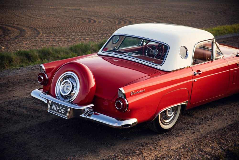Vintage red Thunderbird car on dirt road at sunset.