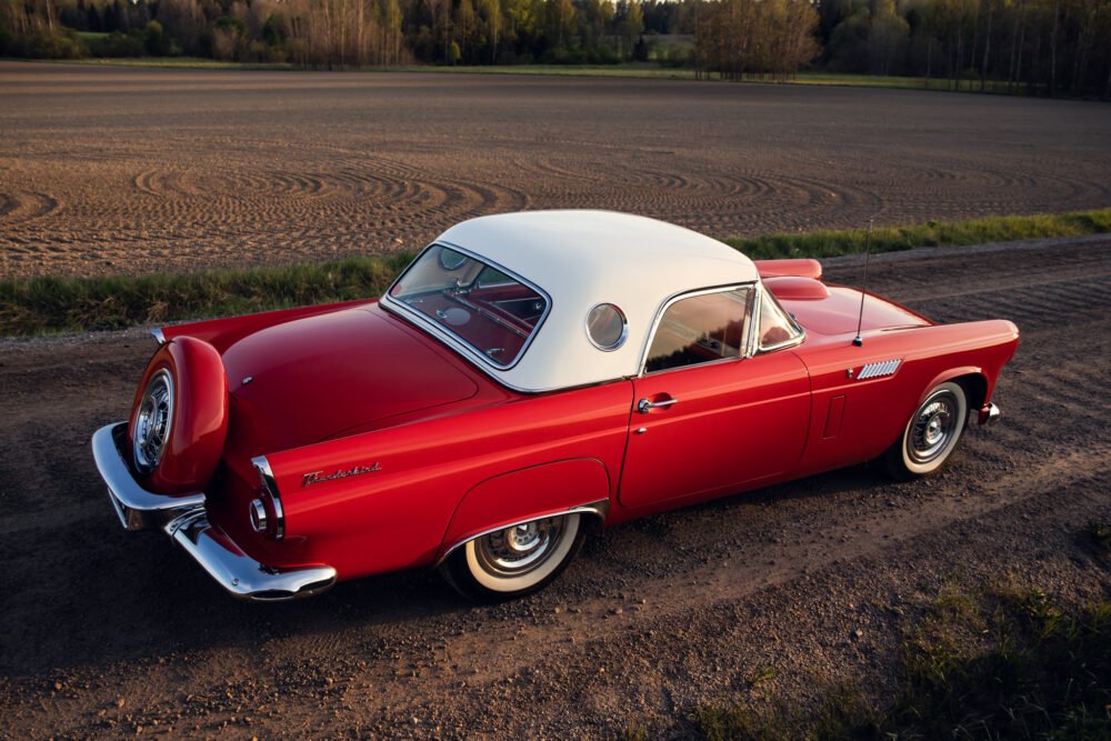 Vintage red Thunderbird car parked in rural field.