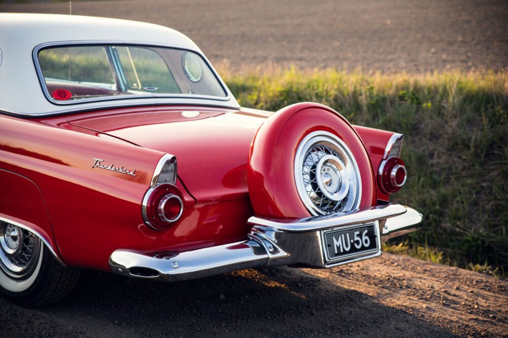 Red vintage Thunderbird car on countryside road.
