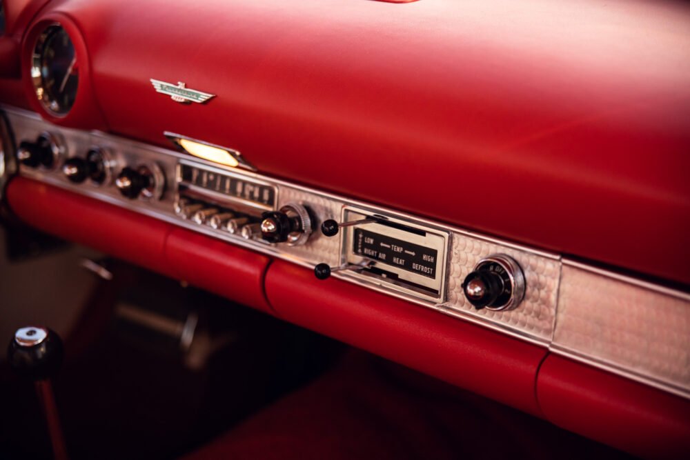Vintage red car dashboard with chrome details and controls.