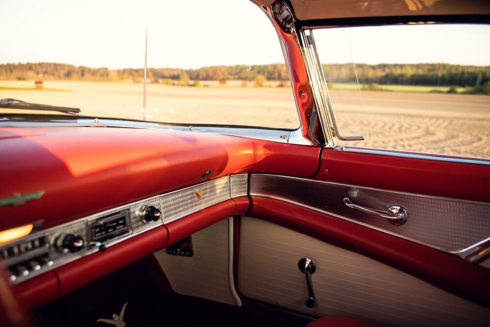 Vintage car interior, red dashboard, sunny field view.